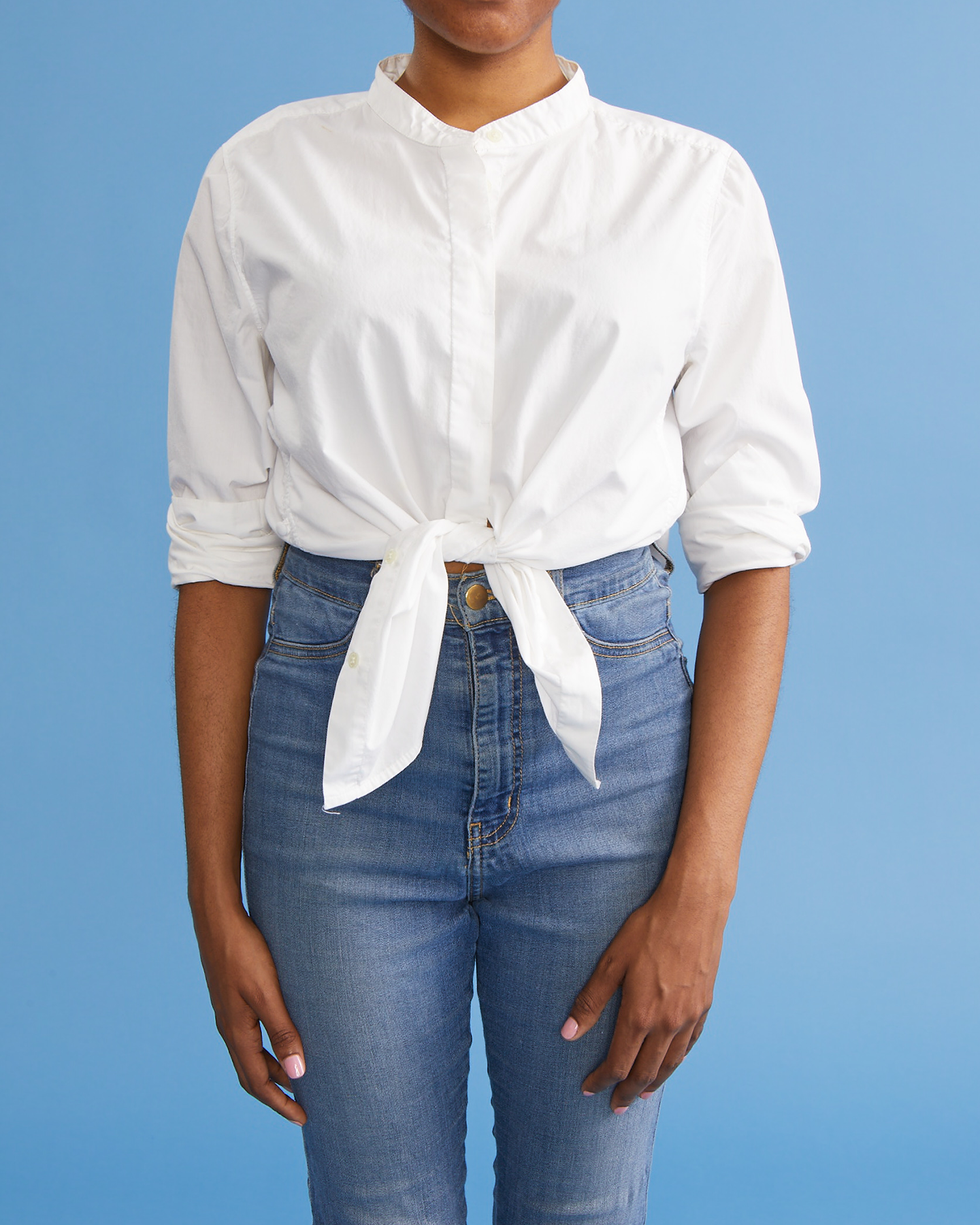 how to tie a shirt knot, woman wearing a white button down shirt with hands at her sides while wearing jeans