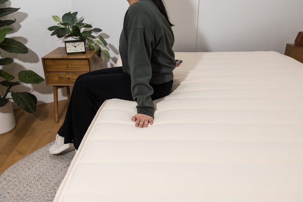 a woman sits on the edge of a cream mattress