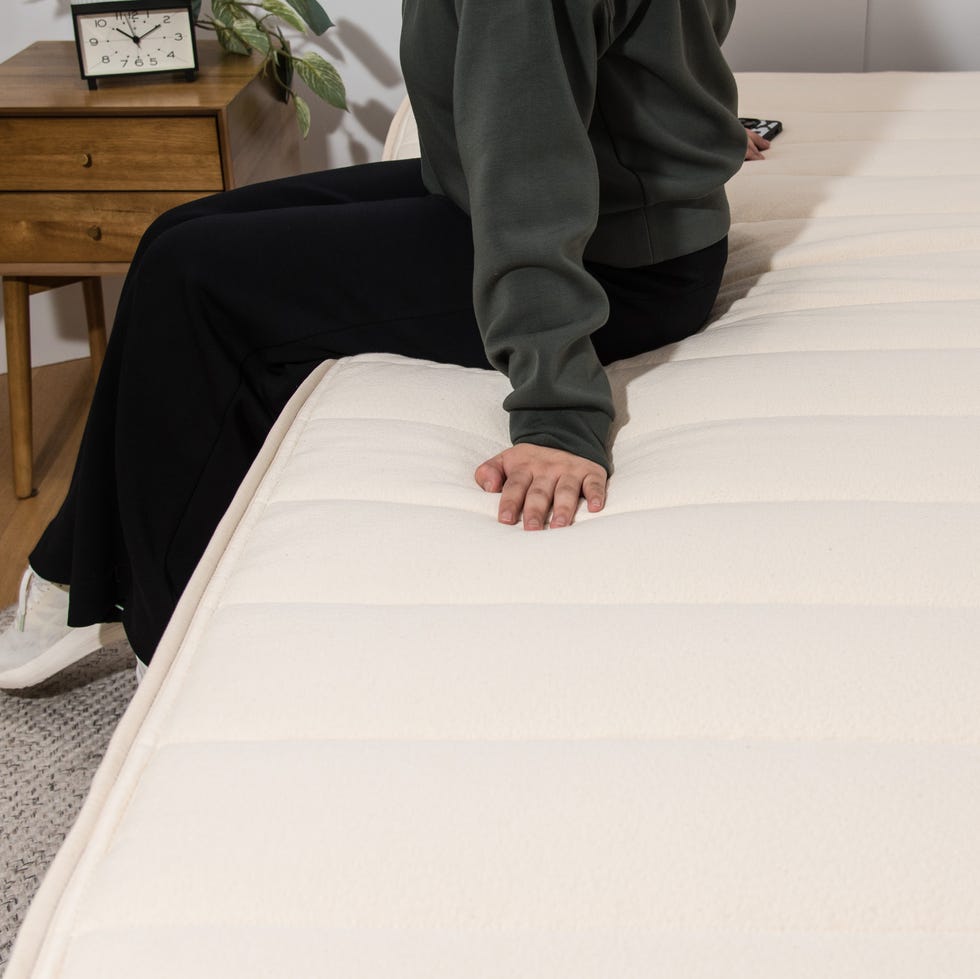 best mattresses in a box- how we test a woman sits on the edge of a cream mattress