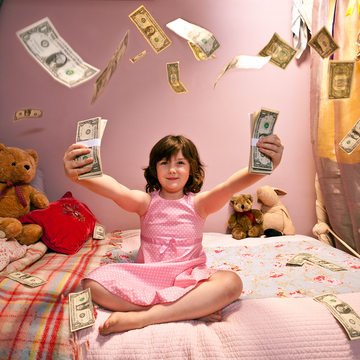 a young girl sitting on her bed in a pink dress with stuffed animals and dollar bills flying all over