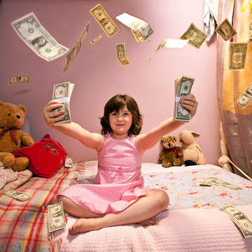a young girl sitting on her bed in a pink dress with stuffed animals and dollar bills flying all over