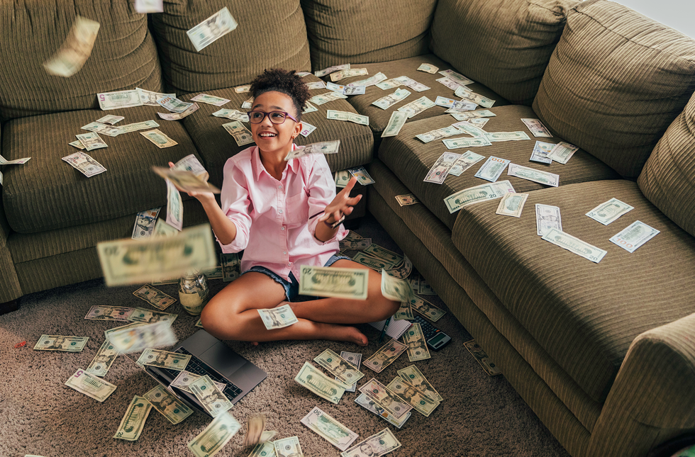 young girl sitting on the floor in front of a couch throwing dollars in the air