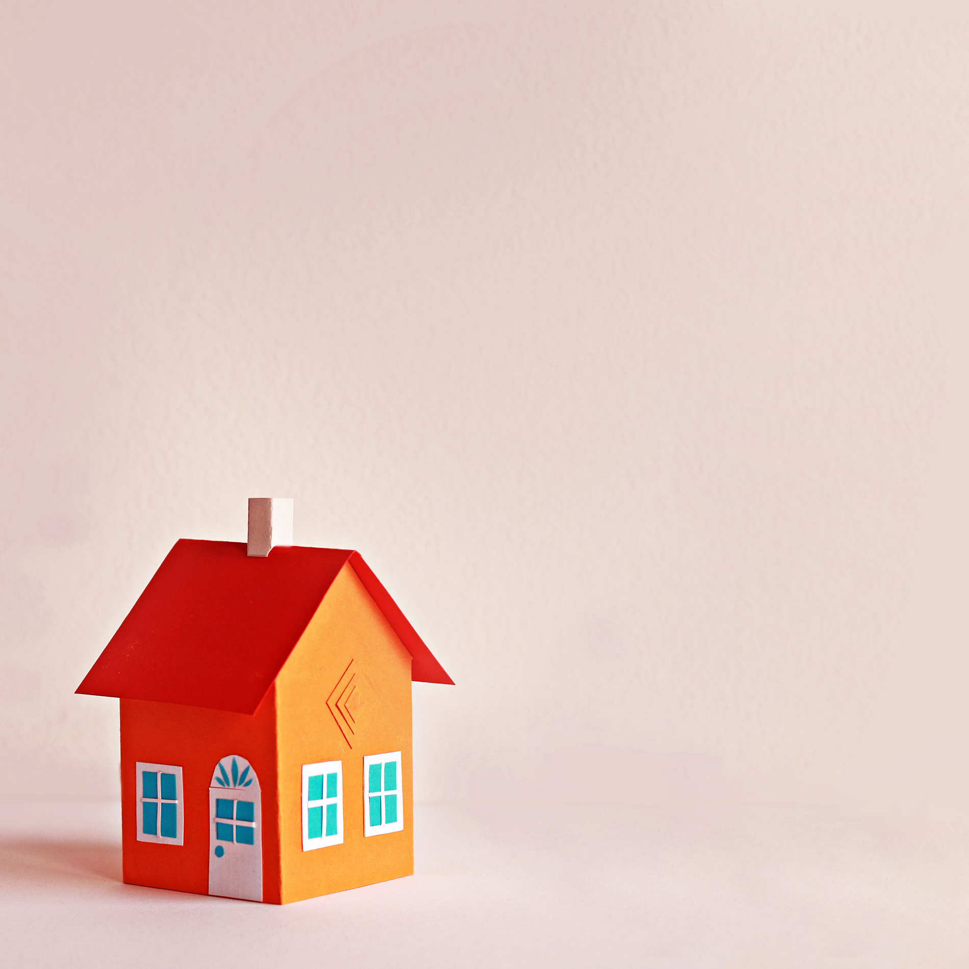 small orange paper house with blue windows on pink background