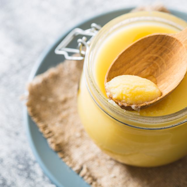 ghee or clarified butter in jar and wooden spoon on gray table. top view. copyspace. ghee butter have healthy fat and is a common cooking ingredient in many of the indian food