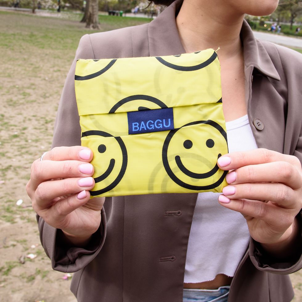 a model with pink nails holding a folded yellow with smiley faces baggu standard baggu tote bag, good housekeeping's testing for best tote bags