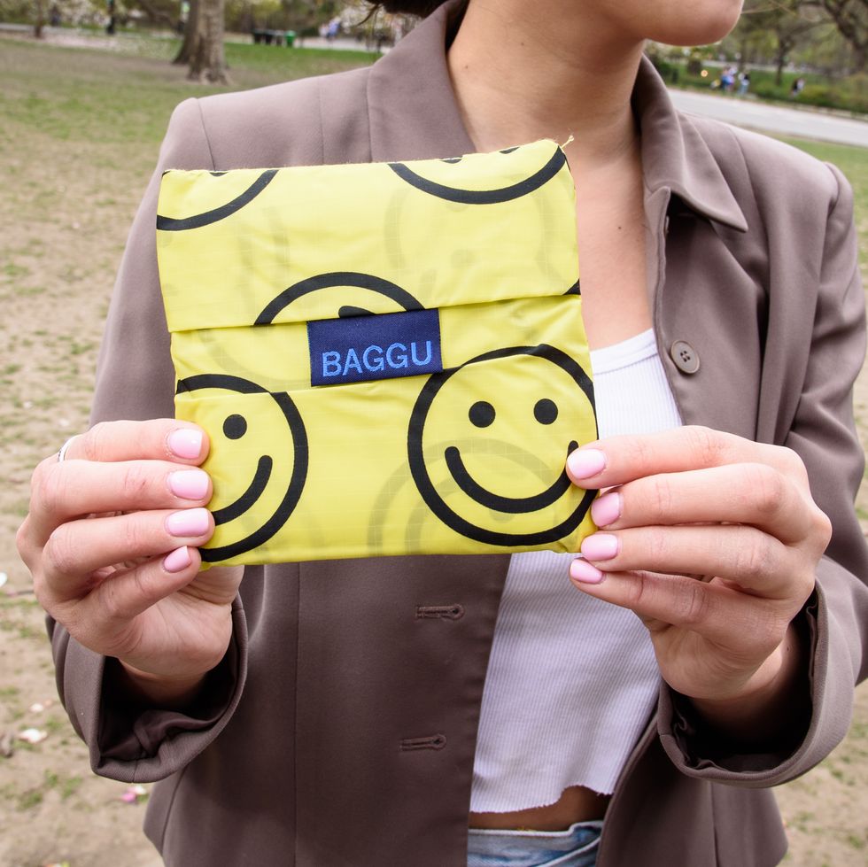 a model with pink nails holding a folded yellow with smiley faces baggu standard baggu tote bag, good housekeeping's testing for best tote bags