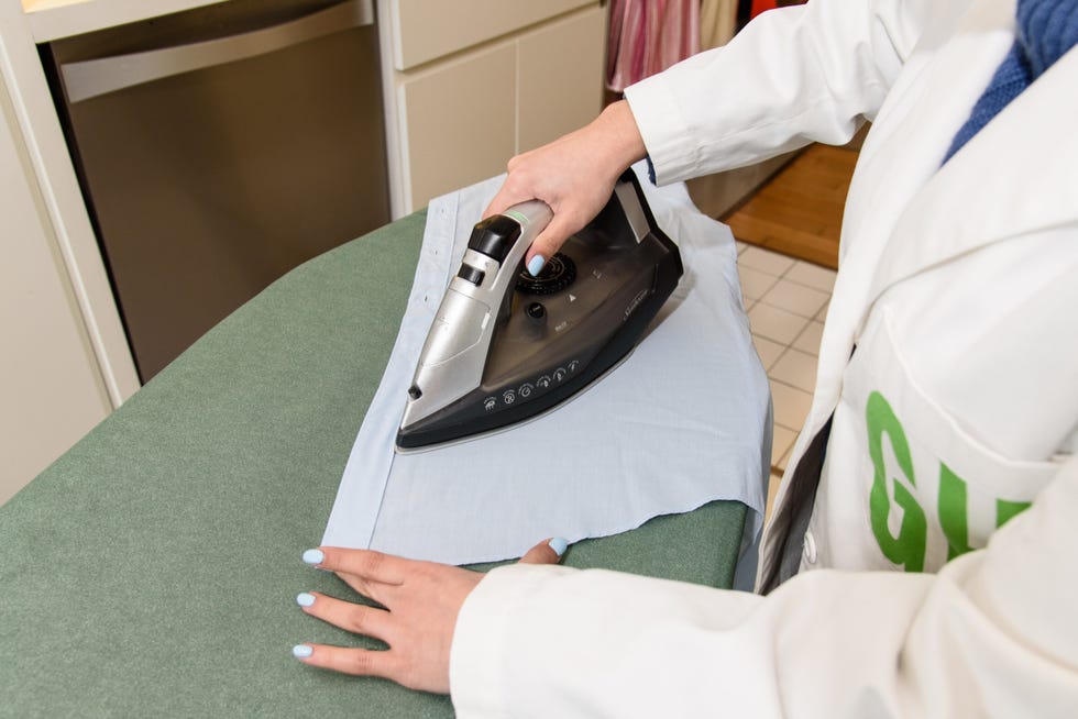 ironing a light blue shirt on a green ironing board