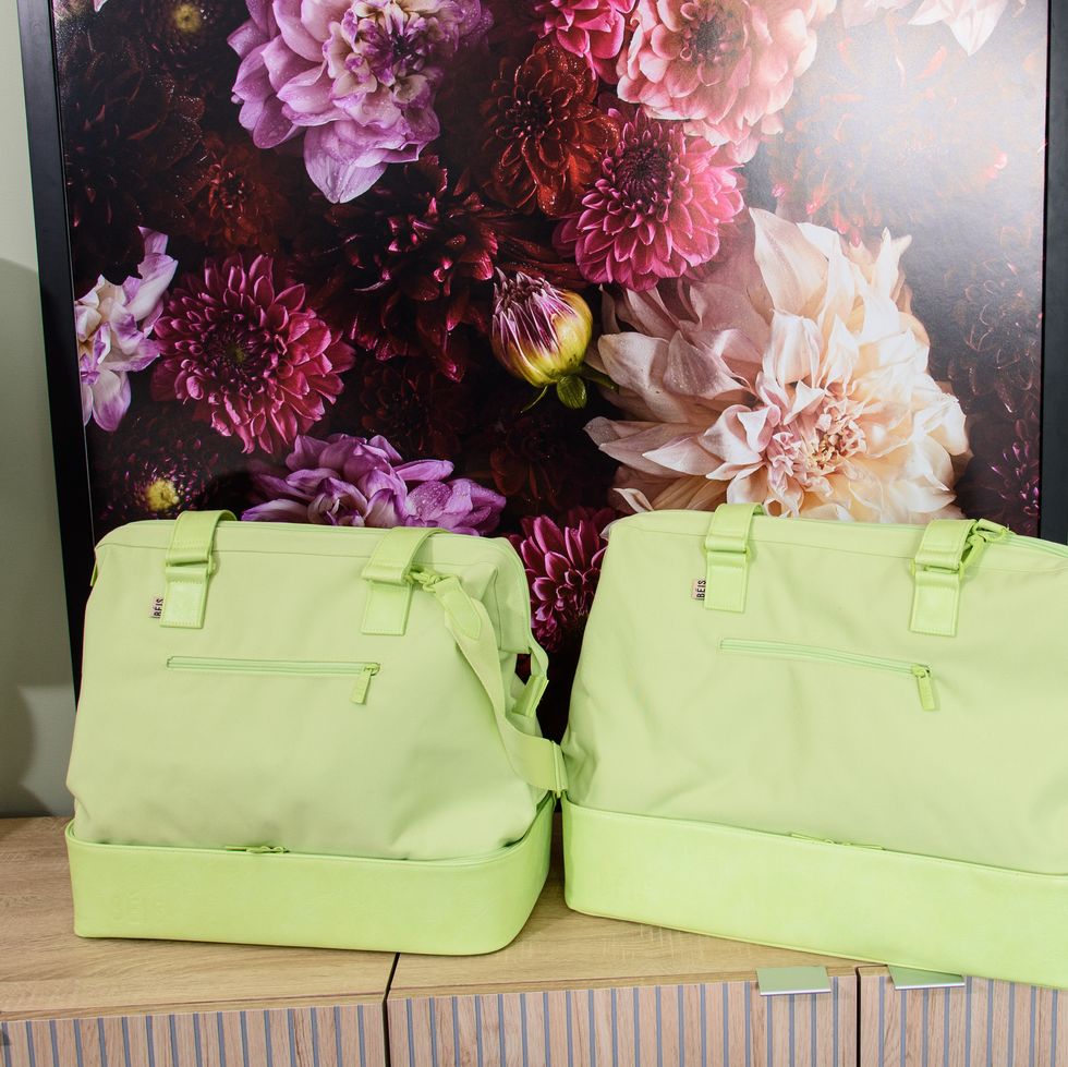 two lime green beis weekender bags, one mini and one original, next to each other in front of a floral image, good housekeeping's best weekender bags testing