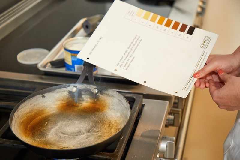 a person holding a browning color chart above a carbon steel pan during a heat distribution test