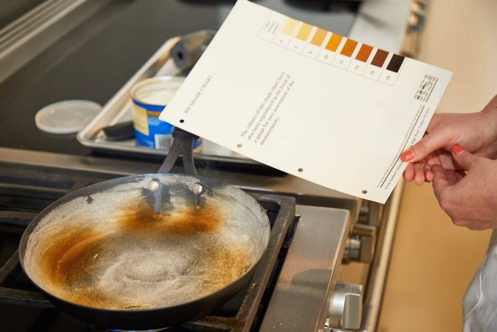 best carbon steel skillets a test kitchen expert holds a browning chart over a pan on the stove to determine the level of browning in the pan that is coated in cooked flour
