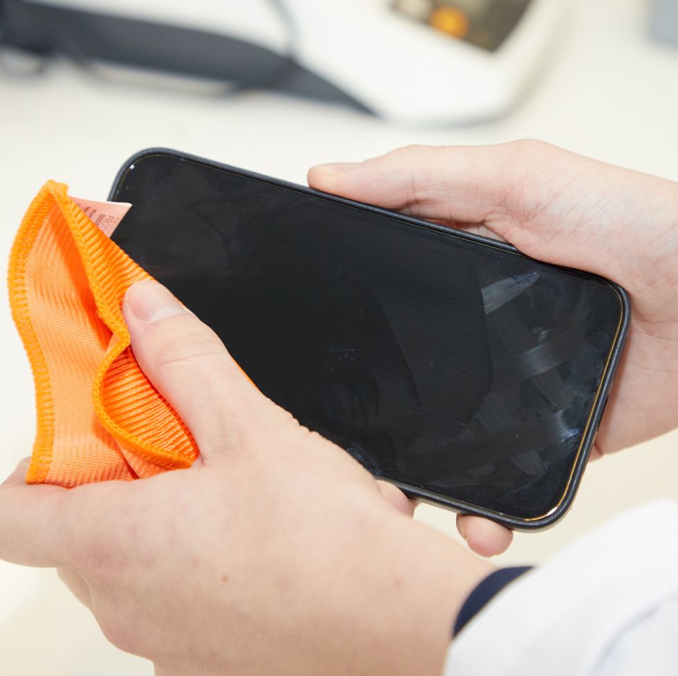 a hand wiping a black smart phone with an orange cloth