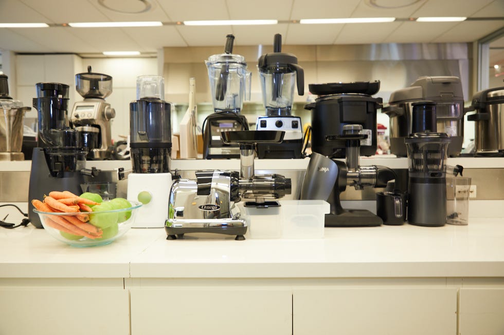 multiple juicers being tested with carrots and apple on countertop