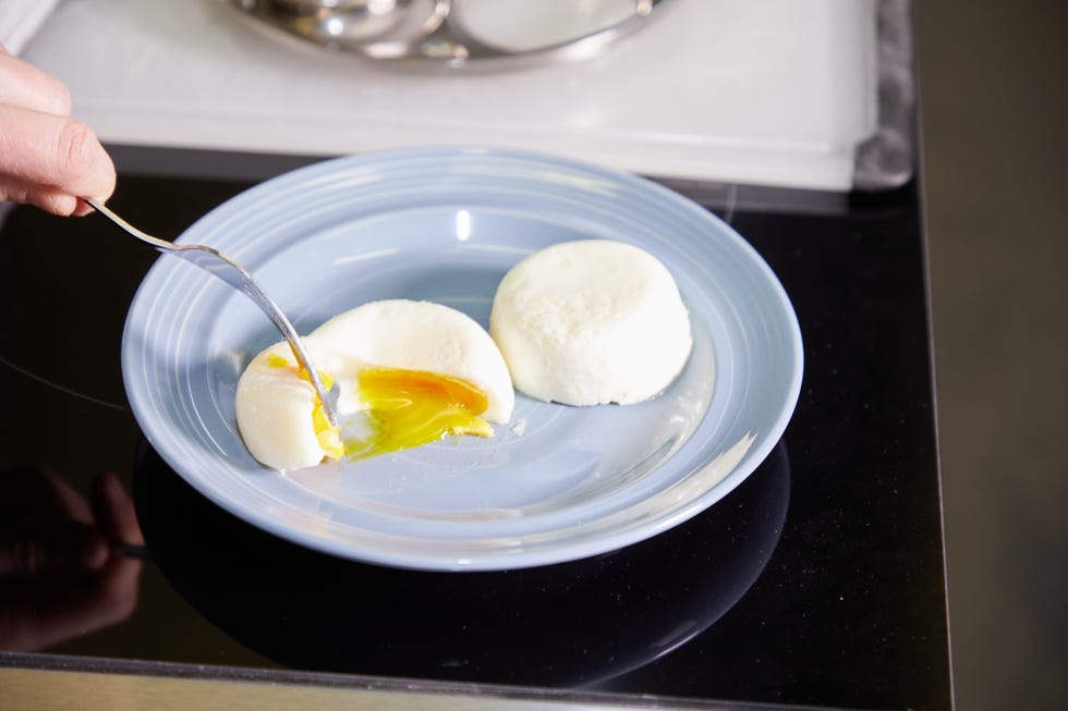 two poached eggs on plate with one being cut open with a fork to show the runny yolk