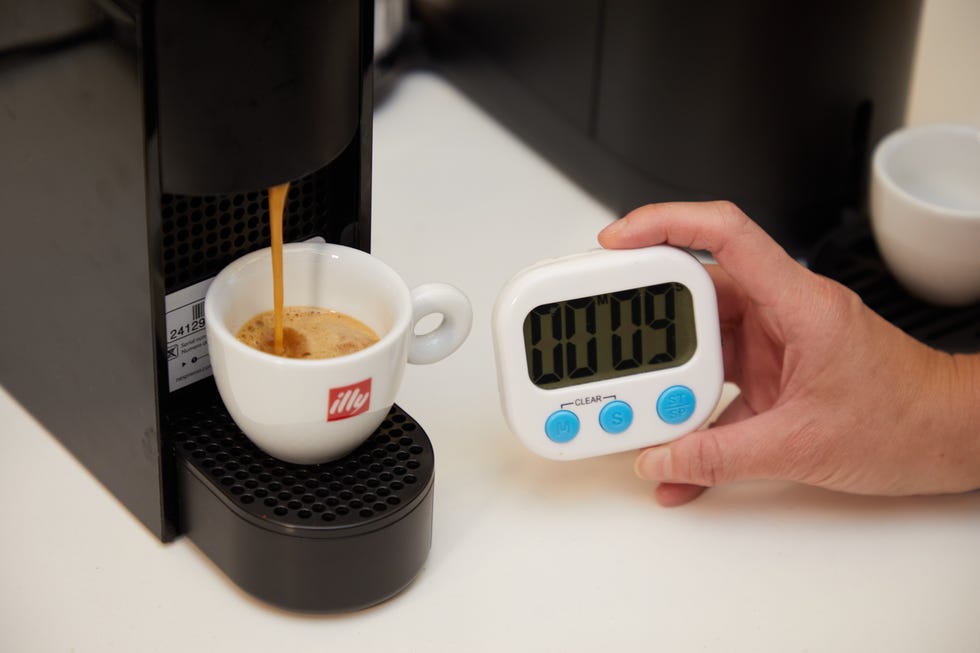 machine brewing espresso into a cup and a hand holding a timer