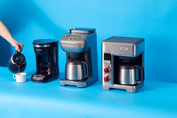 a person pouring coffee into a mug with three coffee makers