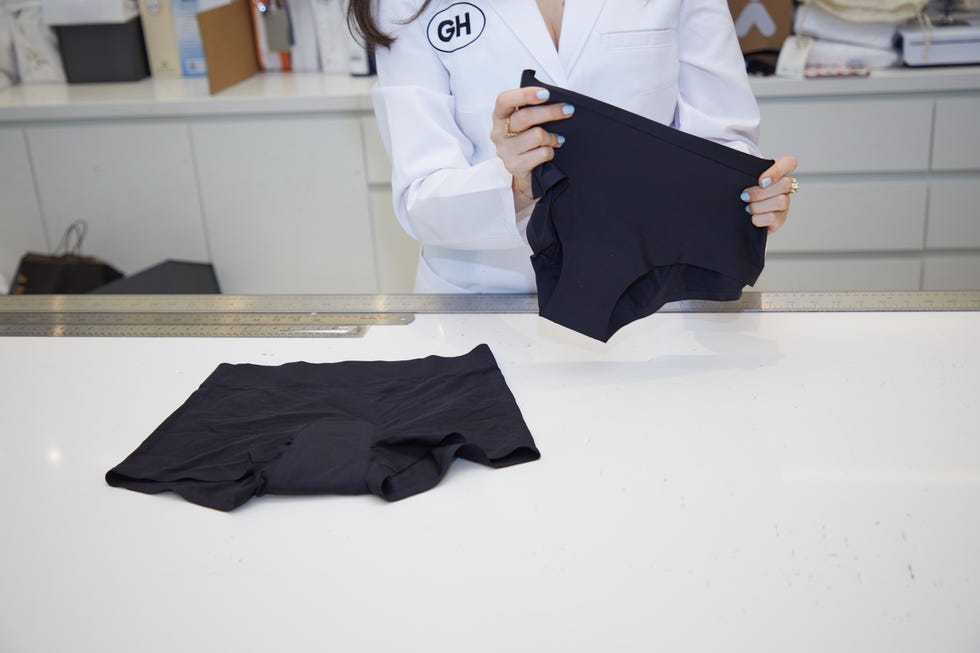 a good housekeeping analyst holding up a black pair of kt by knix leakproof underwear with the black sleep shorts on the lab bench, good housekeeping's best period underwear