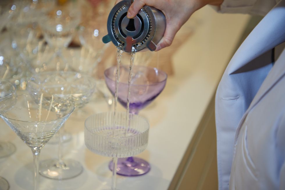 a person pouring a martini into glasses