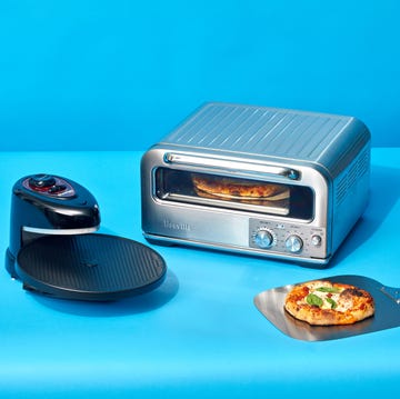 two pizza ovens side by side with a pizza on a peel and in one of the ovens