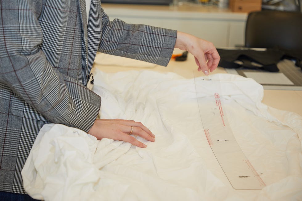 a textiles lab analyst measuring shrinkage of a fitted white sheet with an astm standardized tool