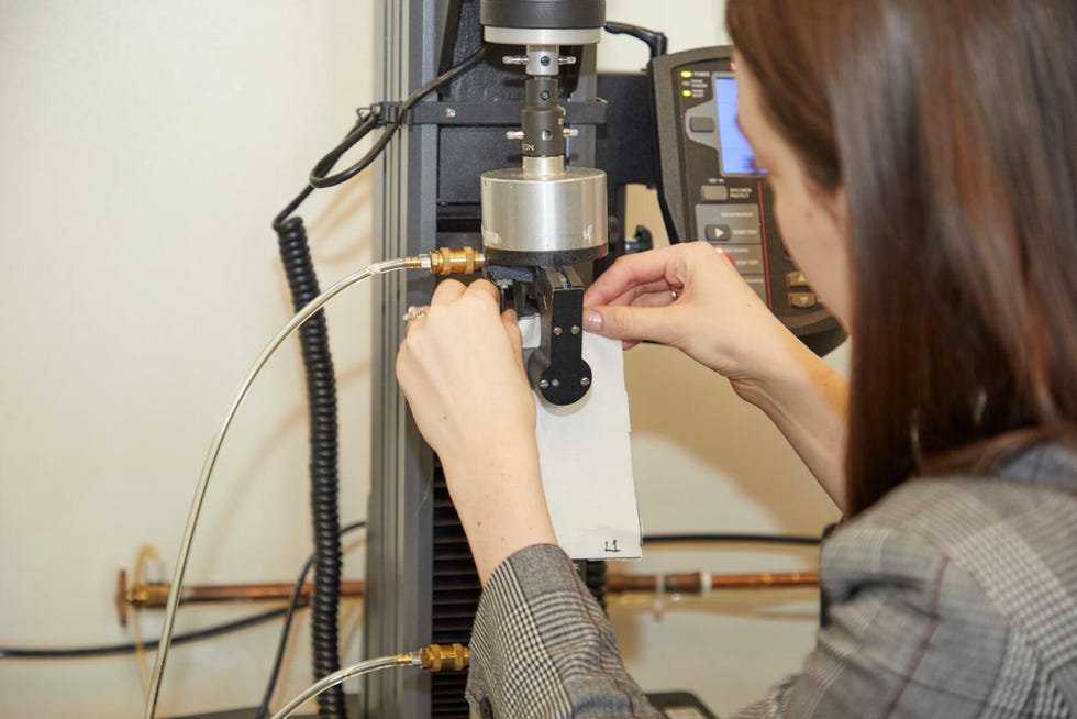 a textiles lab analyst placing a white swatch of a sheet into the clamps of an instron machine for strength testing