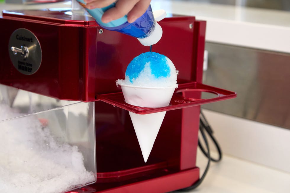 hand pouring blue raspberry syrup on a snow cone in the holder of an ice shaving machine