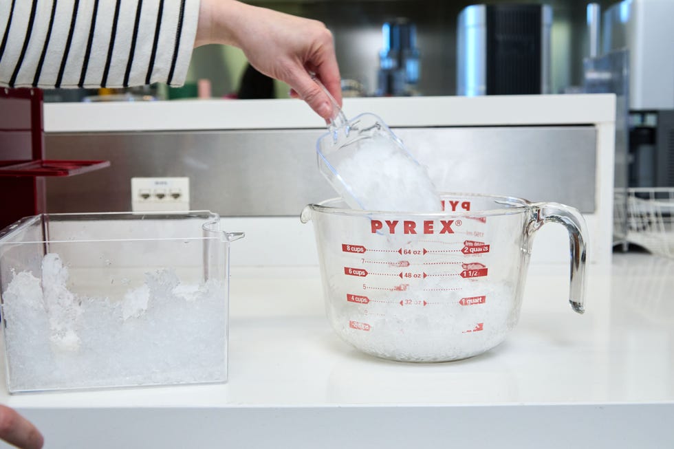 hand scooping shaved ice from a bin into a large glass measuring cup