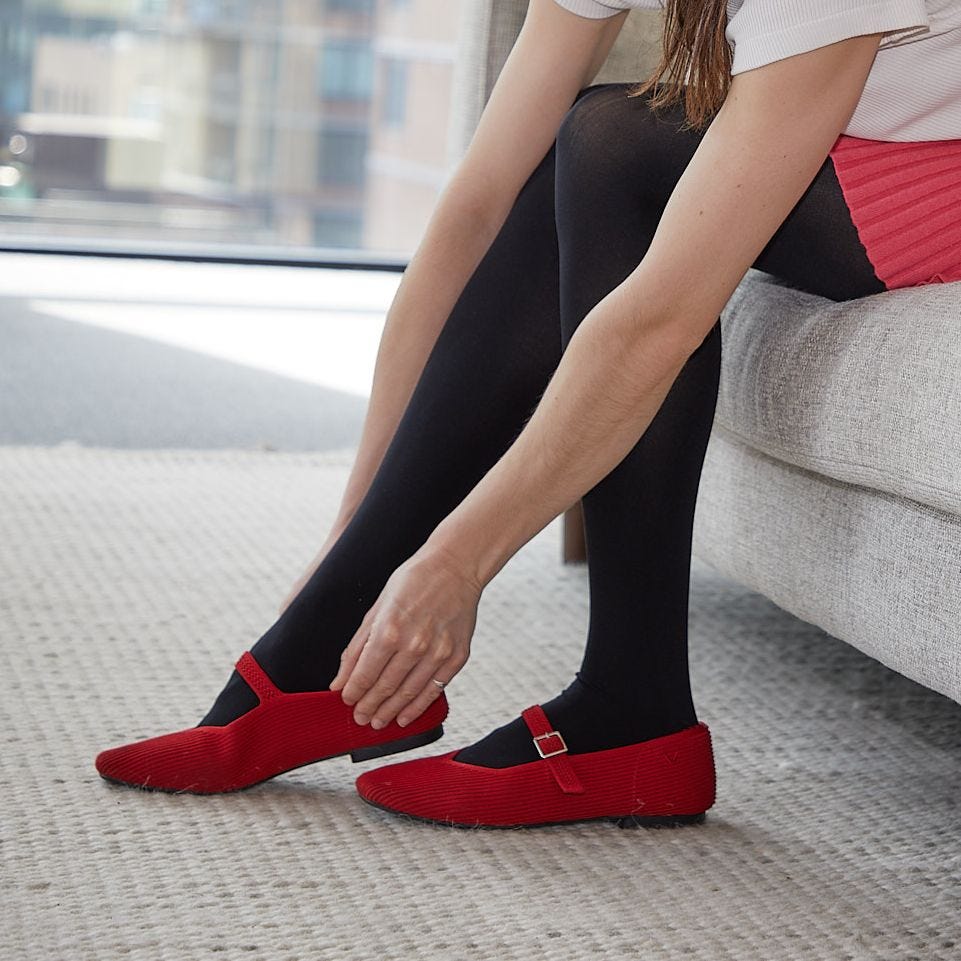 a person modeling red mary janes from vivaia against a grey carpet and grey couch