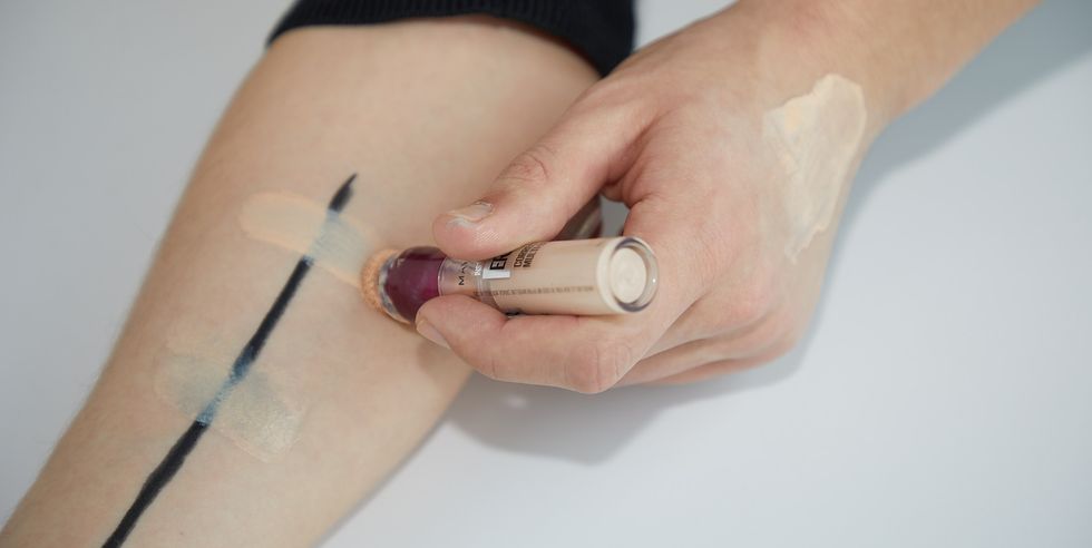 a medium coverage and sheer coverage concealer being swatched on top of an arm with a stripe of eyeliner on it