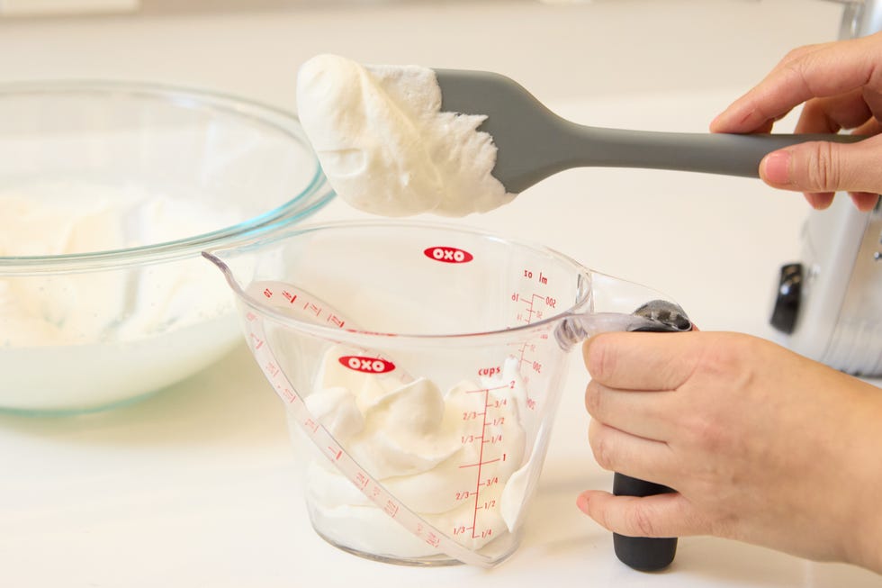 person adding whipped cream into a measuring cup