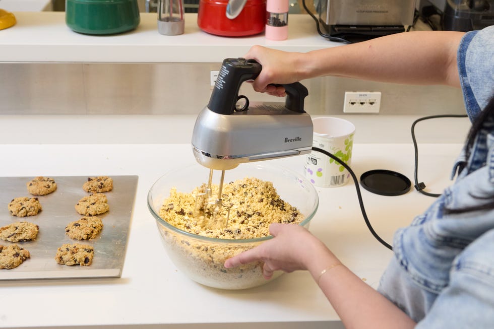 person mixing cookie dough with a hand mixer and baked cookies on a counter