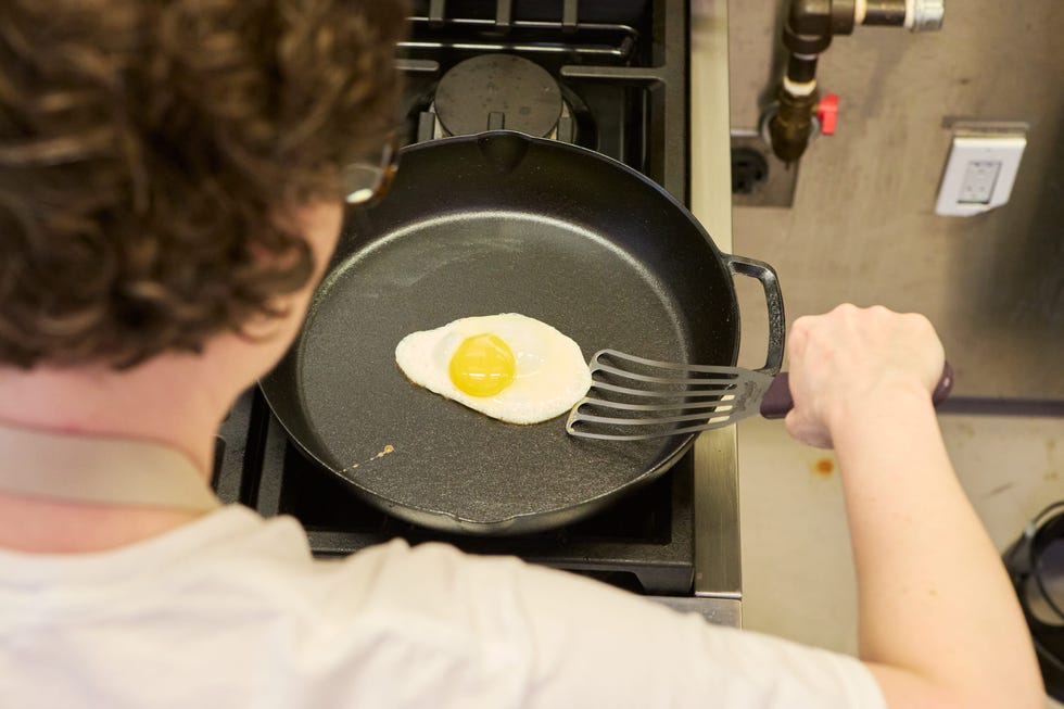 a woman holding a spatula about to flip a fried egg in a cast iron skillet