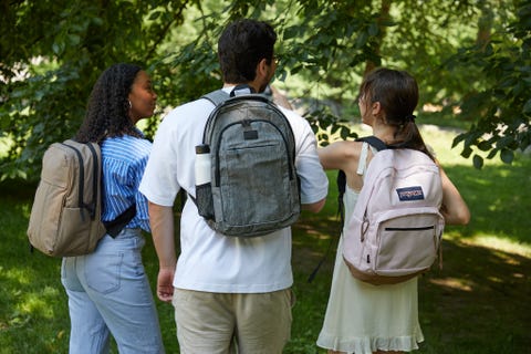 a group of three students wearing backpacks on a campus, good housekeeping's best college backpacks
