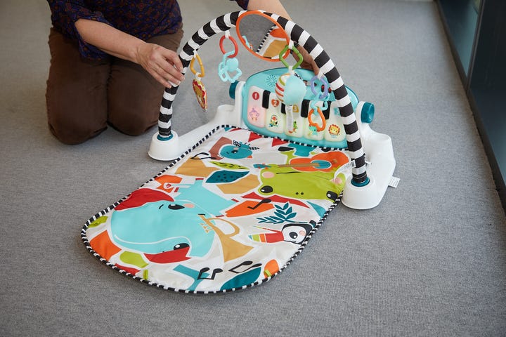 a good housekeeping lab staffer kneels on the floor and tests how hard you have to press the keys of the fisher price kick and play to make them light up, part of testing baby play gyms
