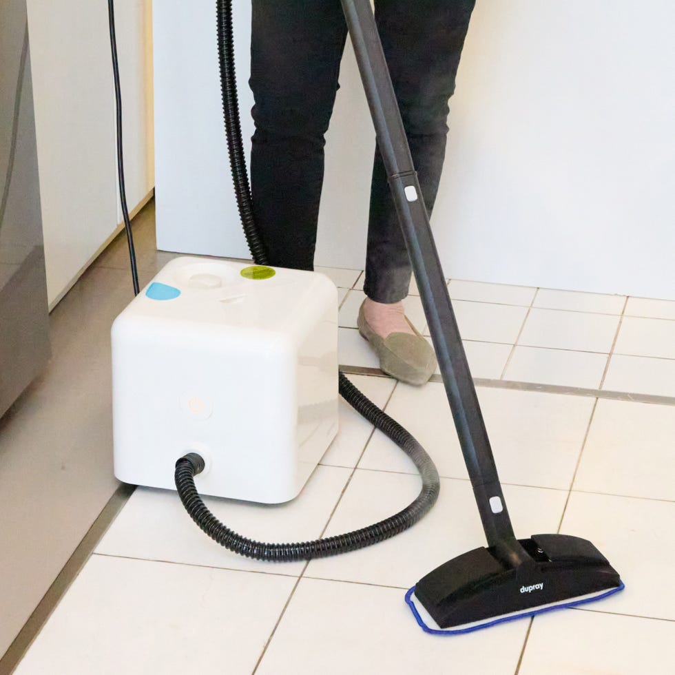 white steam cleaner with black hose on a white tiled floor