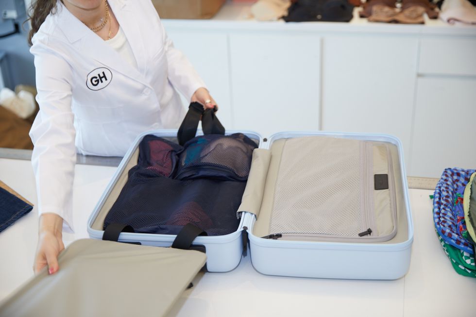 an analyst putting navy away insider packing cubes in a carry on suitcase, good housekeeping's best packing cubes