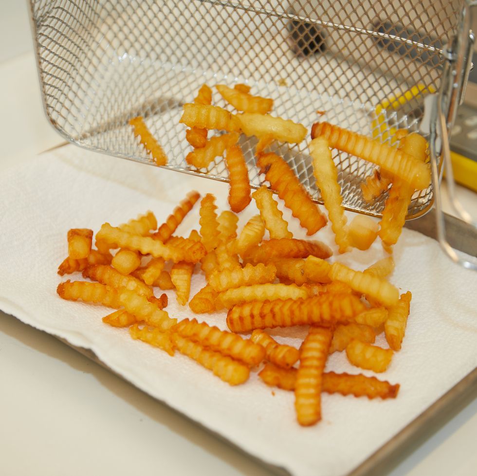 golden french fries falling from a fryer basket onto a paper towel lined tray