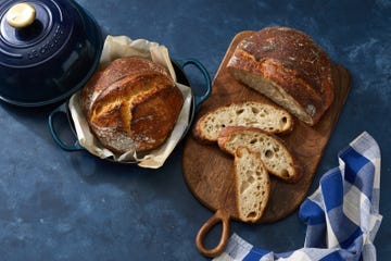 two loafs of sourdough, one in a cloche and one sliced on a cutting board