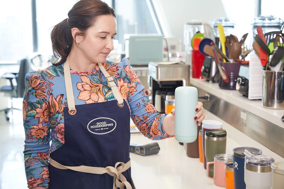 person holding a light blue insulated tumbler in a kitchen setting