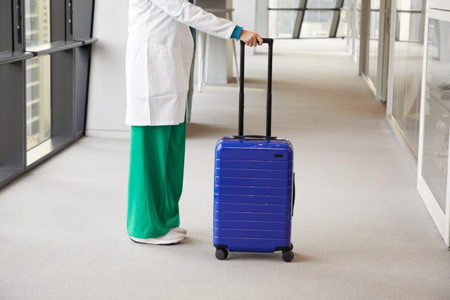 a person standing next to a blue suitcase in a corridor