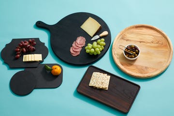 multiple charcuterie boards on a blue background with food such as crackers, grapes, salami, olives and cheese