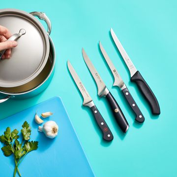 four top tested boning knives next to a stock pot and a cutting board with garlic and herbs