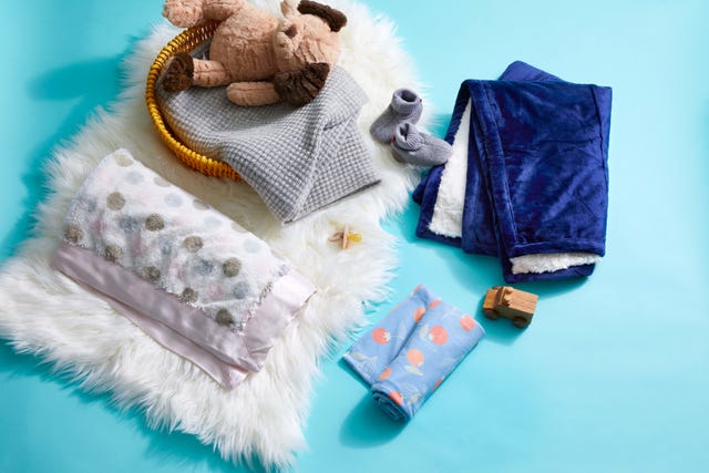 four of the best baby blankets, shown with baby booties and some toys, part of a good housekeeping list of the best tested blankets for babies