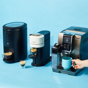 a hand holding a coffee mug shown with coffee and espresso makers