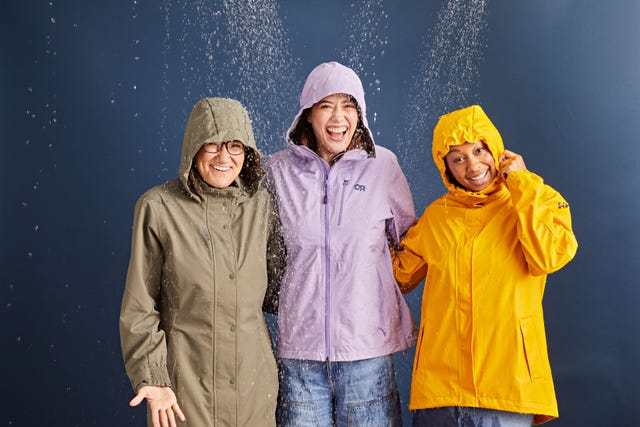 three women wearing rain jackets against a navy blue background with rain falling on them