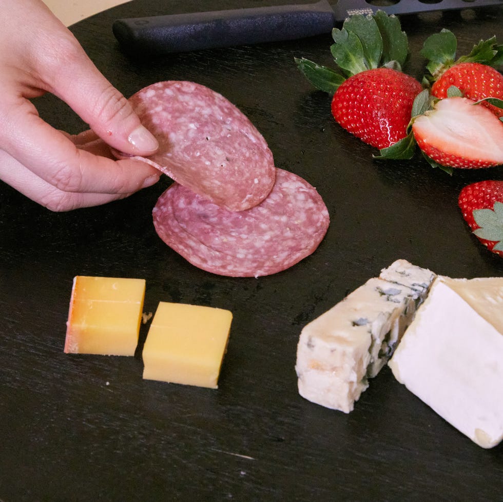 best charcuterie boards person's hand laying salami on a charcuterie board that has cheese and strawberries