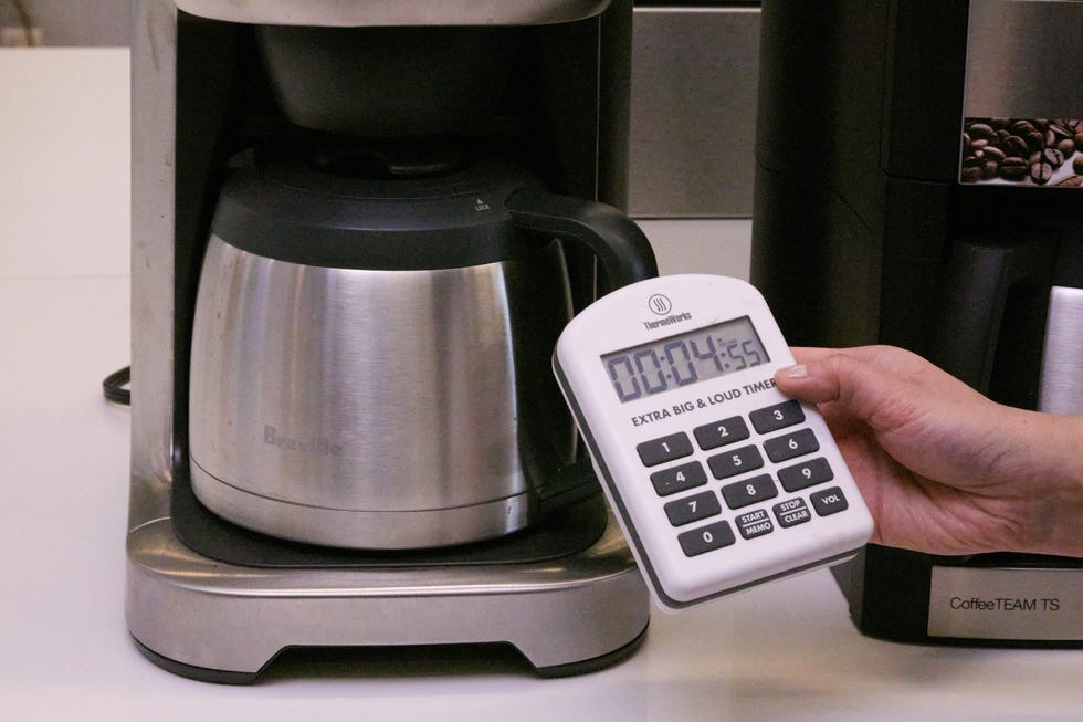 hand holding a timer in front of a drip coffee maker