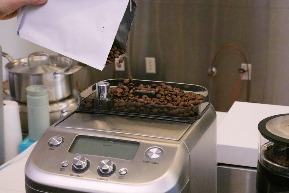 a person is pouring coffee beans into the hopper of a breville coffee machine