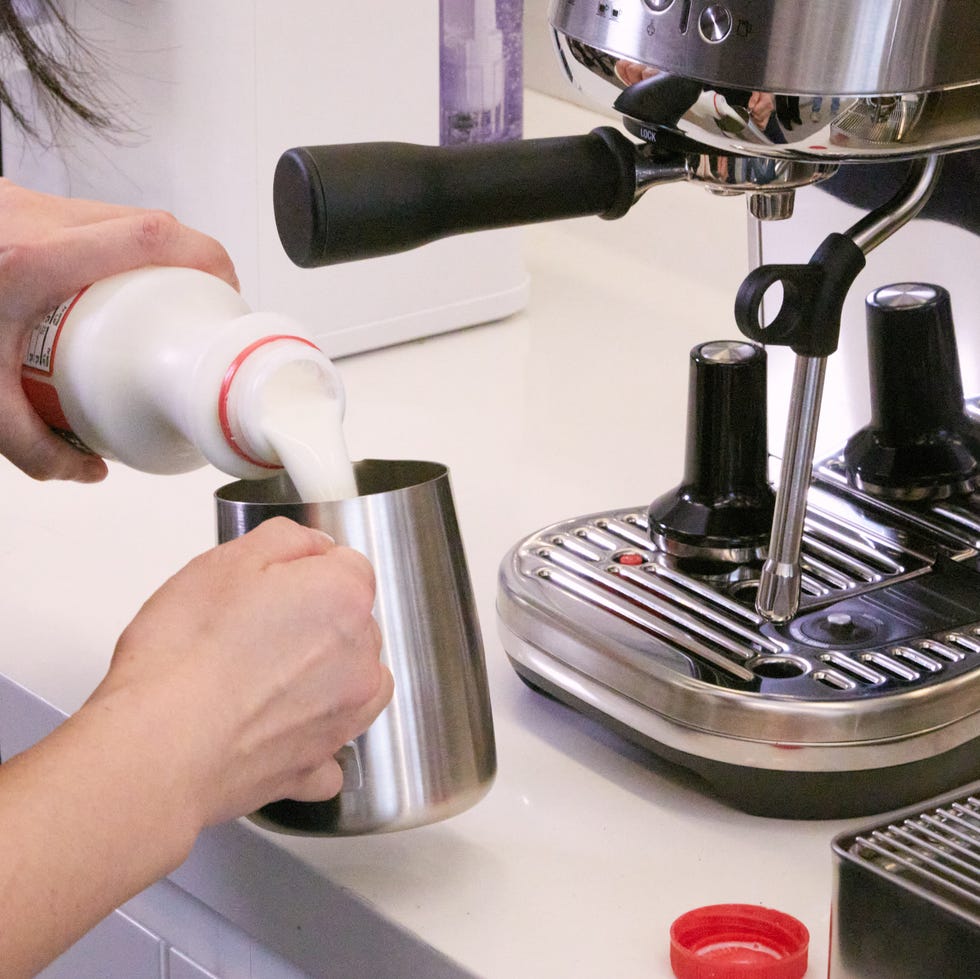 best manual espresso machines person pouring whole milk into a milk frothing pitcher