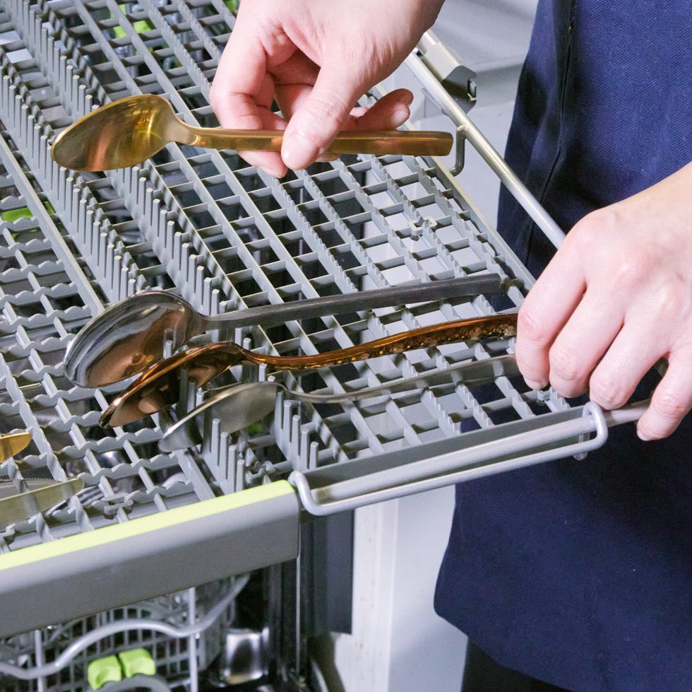 best flatware sets hand putting a spoon in a dishwasher tray with other flatware