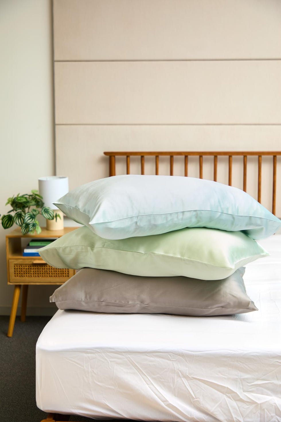 three silk pillowcases in grey, green and blue stacked on top of each other on a bed frame